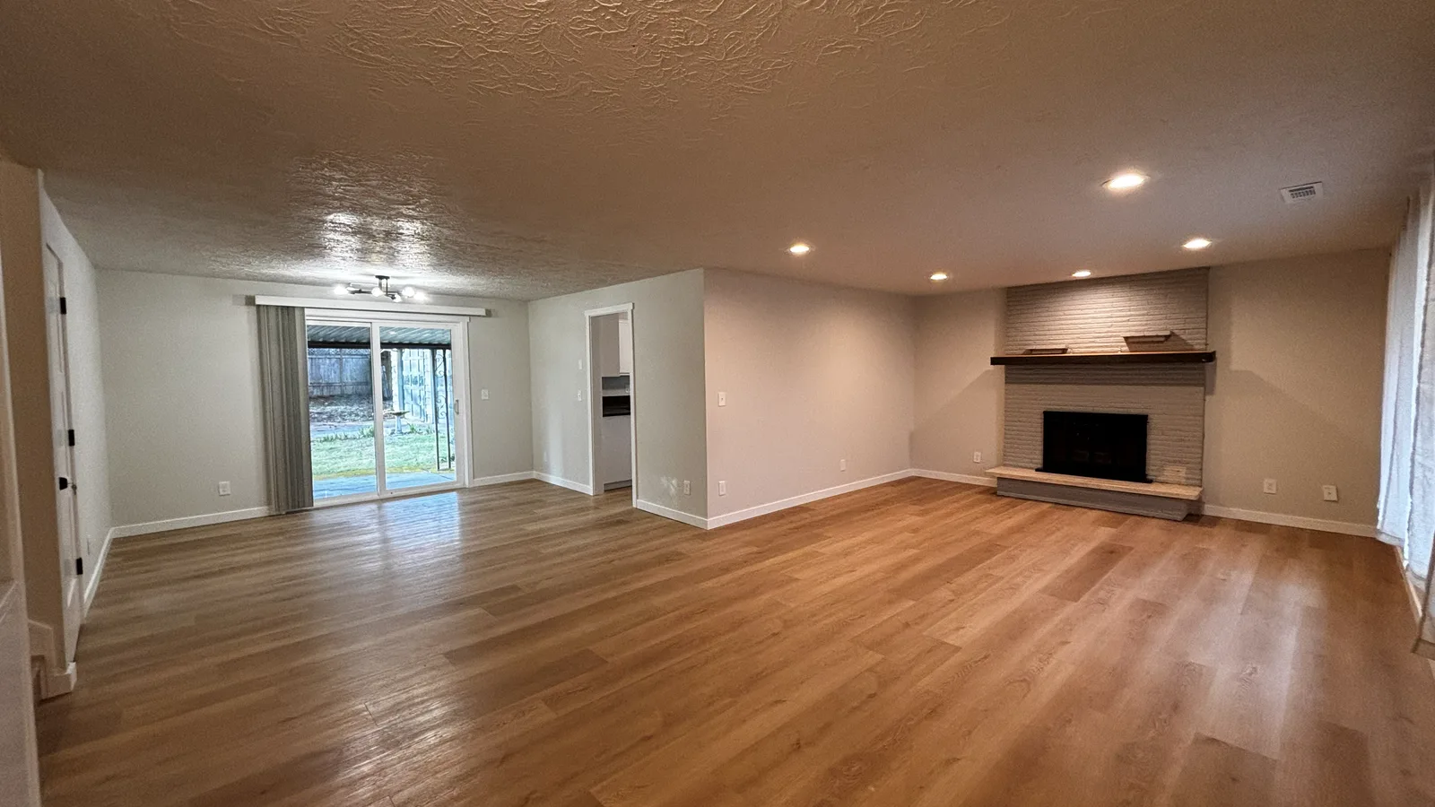 Newly installed hard-surface flooring across an open living room with a brick fireplace in a Clark County home